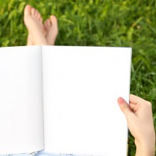 aufgeschlagenes leeres Notizbuch mit der Person, die es in der Hand hält, im Gras sitzend