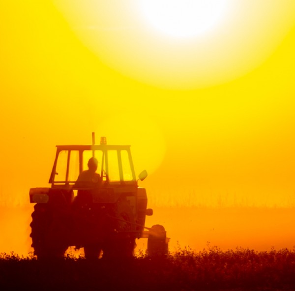 eine Person fährt einen Traktor auf einem Feld mit einem schönen Sonnenuntergang im Hintergrund