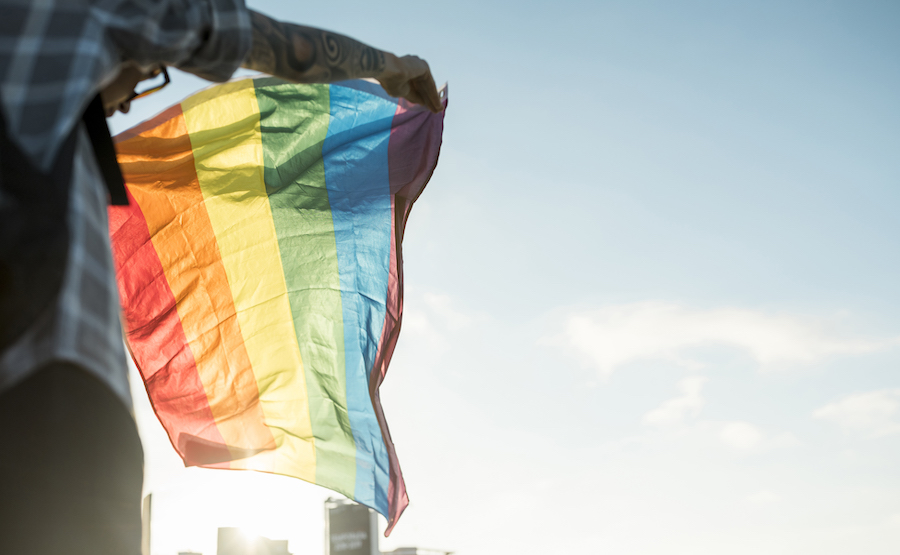 Regenbogenflagge weht im Wind, gehalten von tatowierten Armen