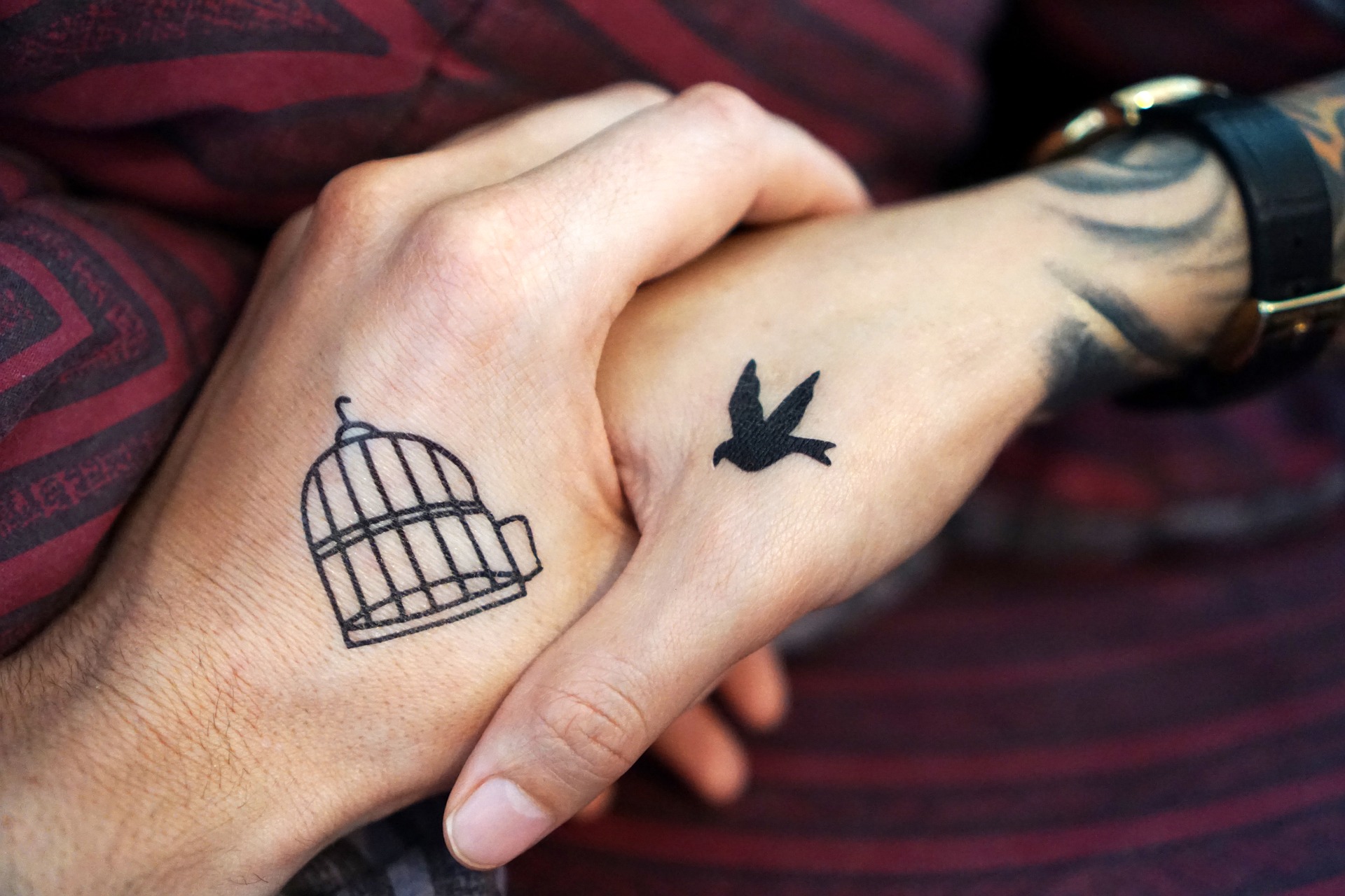 tätowierter Vogel auf einer Hand fliegt in tätowierten Käfig auf anderer Hand